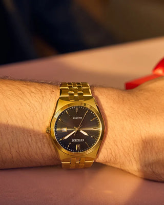 Gold wristwatch with a black dial on a person's wrist, blurred background