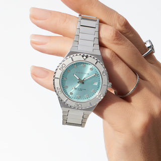 Silver watch with a light blue face held by a hand on a white background