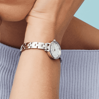Silver watch on a wrist with a light blue background