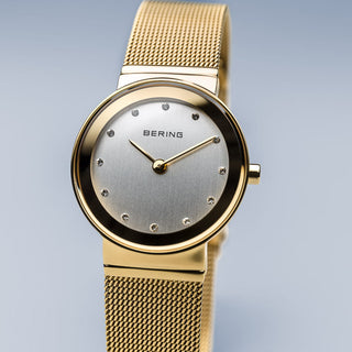 Gold watch with mesh band on a light gray background