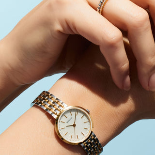 Gold and silver watch on a wrist with a light blue background