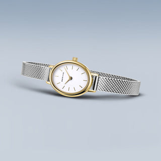 Watch with silver mesh band and gold case on a light gray background