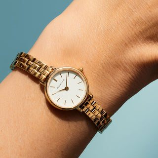 Gold watch on a wrist with a light blue background