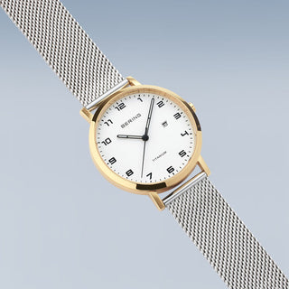 Gold and silver watch with mesh band on a light gray background