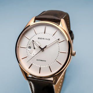 Bering watch with brown leather strap and rose gold case on a light blue background