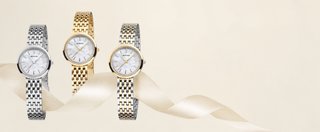 Three watches in silver, gold, and stainless steel on a beige background
