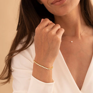 Woman wearing a gold bracelet and necklace against a beige background