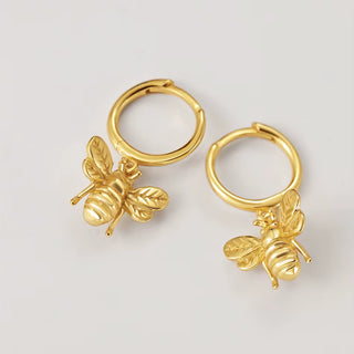 A pair of gold hoop earrings with dangling bee charms, displayed on a clean light gray background.