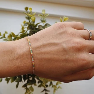 Hand wearing a bracelet with a blurred green plant in the background