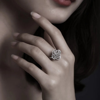 Close-up of a hand wearing a silver ring with intricate design, against a dark background.
