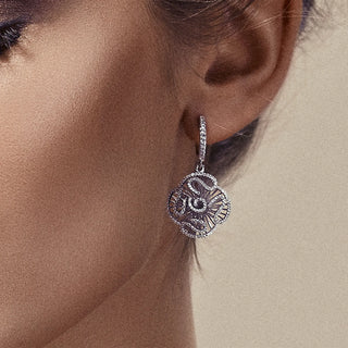 Silver floral earring worn by a person on a neutral background
