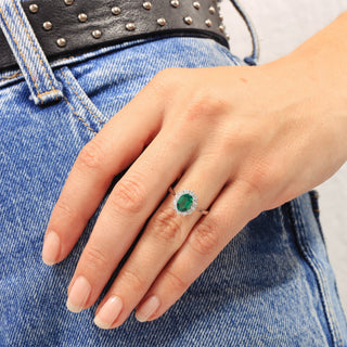 Hand wearing a ring with a green gemstone on blue denim background