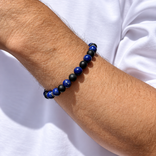A beaded bracelet worn on a person's wrist, featuring alternating glossy royal blue beads and matte black beads, set against a white t-shirt.