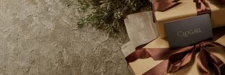 Gift box with a brown ribbon and Clogau card on a textured surface with greenery.