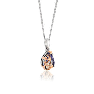 An 18ct gold Tree of Life pendant featuring a tanzanite gemstone with intricate filigree work and small sparkling diamonds, attached to a silver chain.