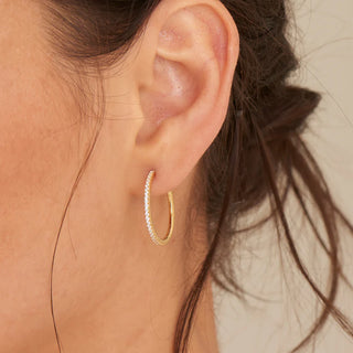Close-up of an ear wearing a gold hoop earring with cubic zirconias.