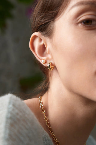 Close-up of a person wearing gold earrings and a necklace with a blurred background