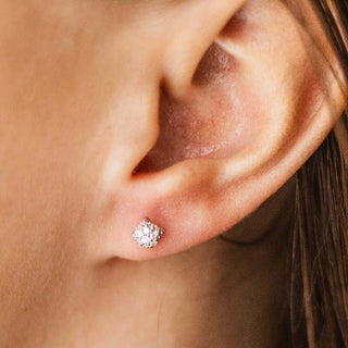 A close-up of a person's ear wearing a small round stud earring with a sparkling clear gemstone in a silver-toned setting.