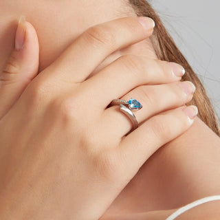 A close-up of a person's hand wearing a silver ring with a marquise-cut blue gemstone.