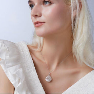 Woman wearing a necklace with a large pendant against a plain background