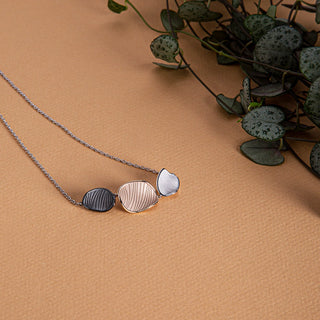 Necklace with three leaf-shaped pendants on a brown surface with green leaves.