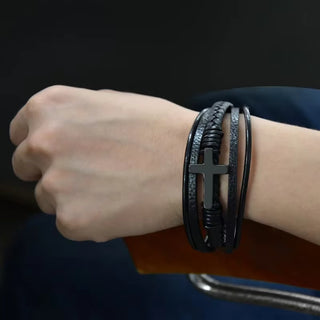 Wrist wearing multiple black leather bracelets with a cross charm on a dark background
