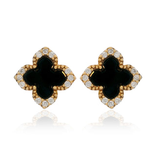 A pair of gold four-leaf clover stud earrings with black enamel centers and clear pavé-set stones, shown on a white background with a soft reflection.