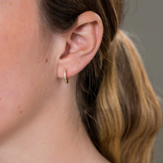Close-up of an ear wearing a gold hoop earring with a blurred background