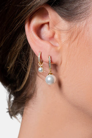 Close-up of an ear wearing gold hoop earrings with pearl accents.