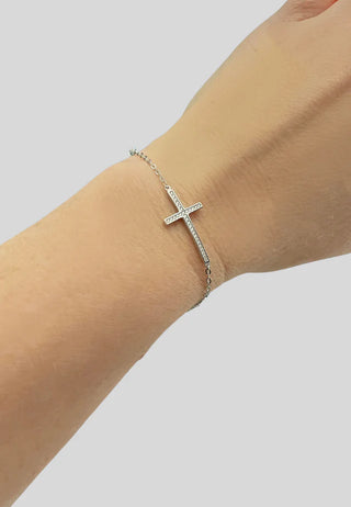 Silver cross bracelet on a wrist against a light gray background
