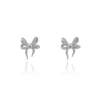 A pair of silver bow-shaped stud earrings with pavé-set clear stones, displayed on a clean white background with soft reflections below.