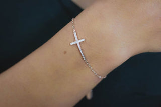 Silver cross bracelet on a wrist against a dark background