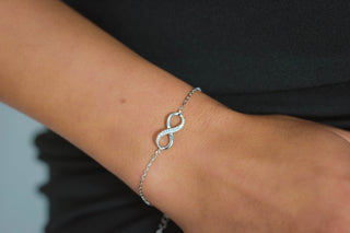 Silver bracelet with an infinity symbol on a wrist against a dark background