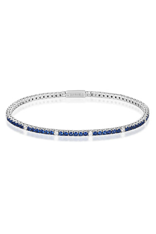 A tennis bracelet featuring deep blue sapphires and small clear stones set in a silver-tone metal, with a visible '' brand engraving on the clasp, shot against a plain white background.