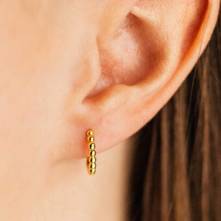 Gold hoop earring worn on a person's ear with a blurred background