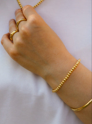 Person wearing gold jewelry including a necklace, ring, and bracelet on a white background