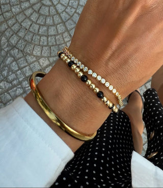 Hand wearing gold bracelets and a ring on a stone pavement background