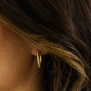 Close-up of a person wearing a gold hoop earring with hair partially covering the frame.