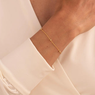 Gold bracelet on a wrist with a light pink blouse