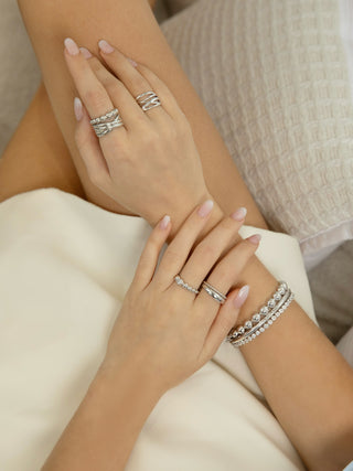 Close-up of hands wearing multiple silver rings and a bracelet on a neutral background