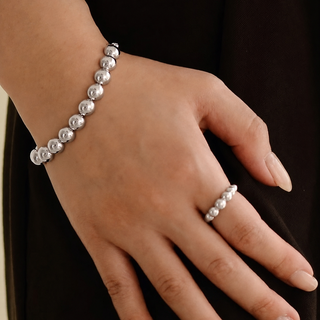 Hand wearing a silver bead bracelet and ring on a dark background