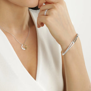 Close-up of a person wearing a silver necklace and bracelet on a plain background
