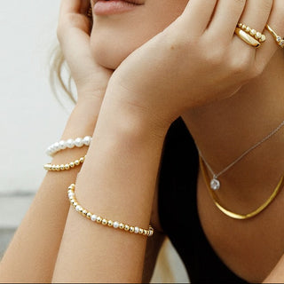 Woman wearing gold jewelry including earrings, necklace, and bracelets against a neutral background