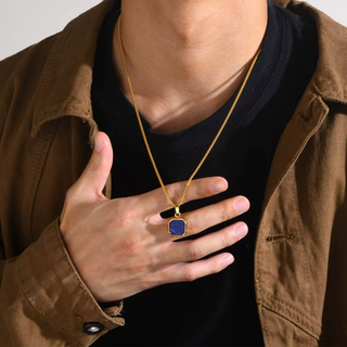 Person wearing a gold necklace with a blue pendant, holding it with their hand.