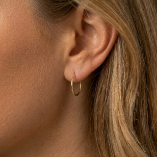 Close-up of an ear wearing a gold hoop earring with blonde hair.