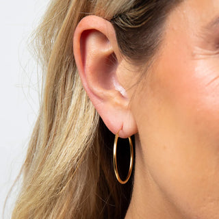 Close-up of a person wearing a gold hoop earring with a plain background