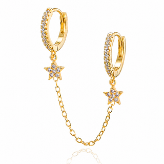 A pair of gold huggie hoop earrings adorned with small clear crystals, featuring dangling star charms connected by a delicate gold chain, shown on a white background.
