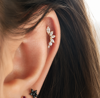 A close-up of a person's ear wearing a gold ear cuff adorned with marquise-cut clear crystals, alongside other small ear piercings.