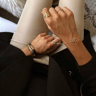 Close-up of hands wearing gold jewelry on a neutral background
