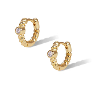 A pair of gold huggie hoop earrings with a twisted rope texture and a small round clear gemstone on each earring, shown on a clean white background.